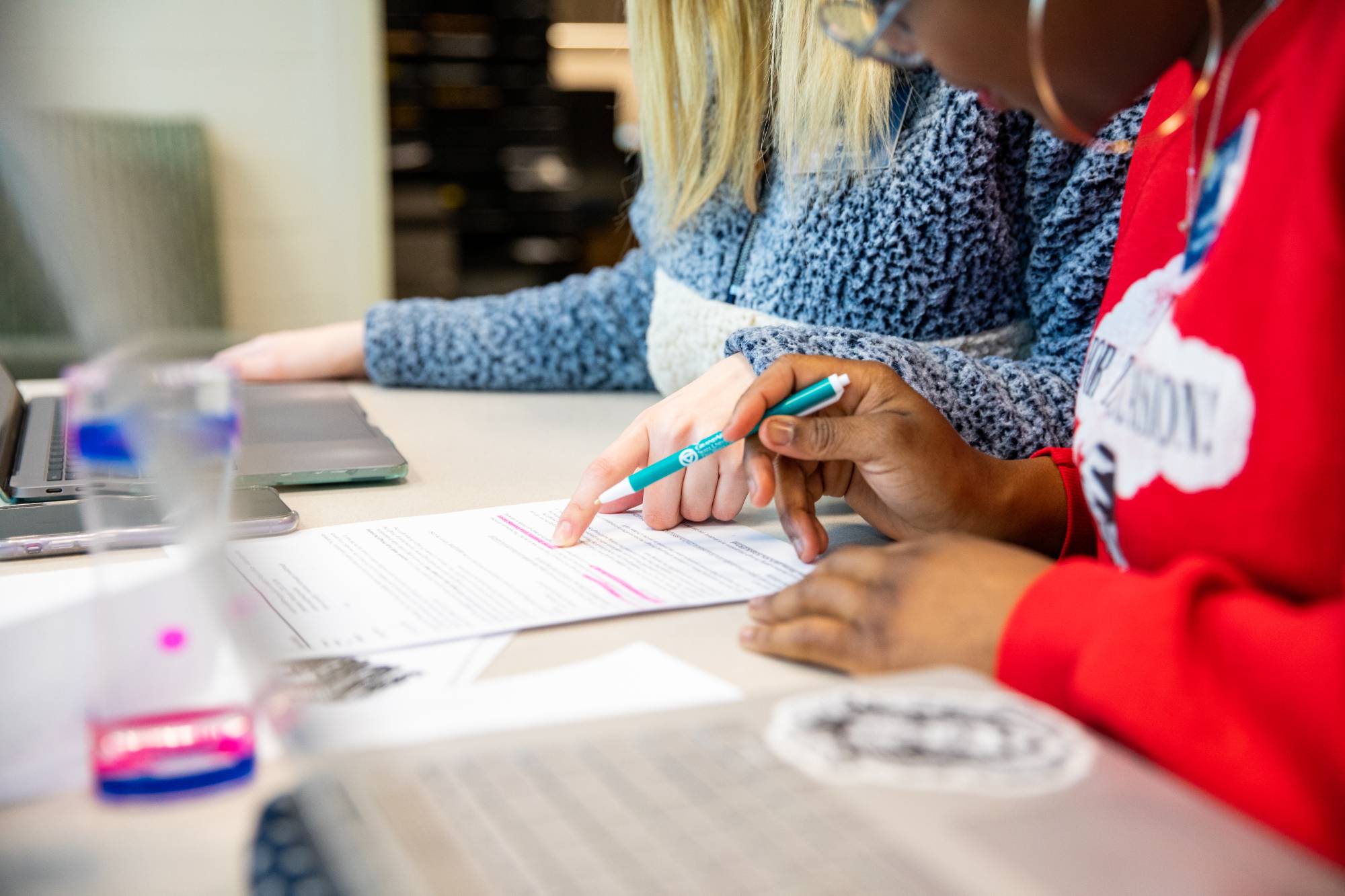 Students working together at a desk on a writing assignment at the writing center, students' chests and hands visible along with their computers
